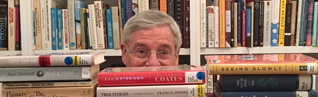 A man with glasses is hiding behind some books.