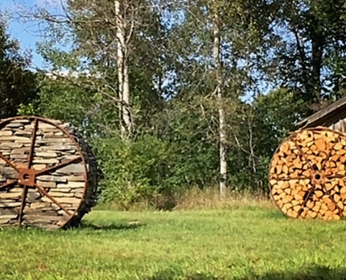 Two large wooden wheels in a field with trees