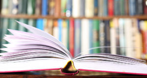 A book is open on the table in front of many books.