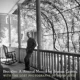 A man sitting on top of a porch next to a tree.