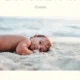 A baby laying on the beach in front of the ocean.